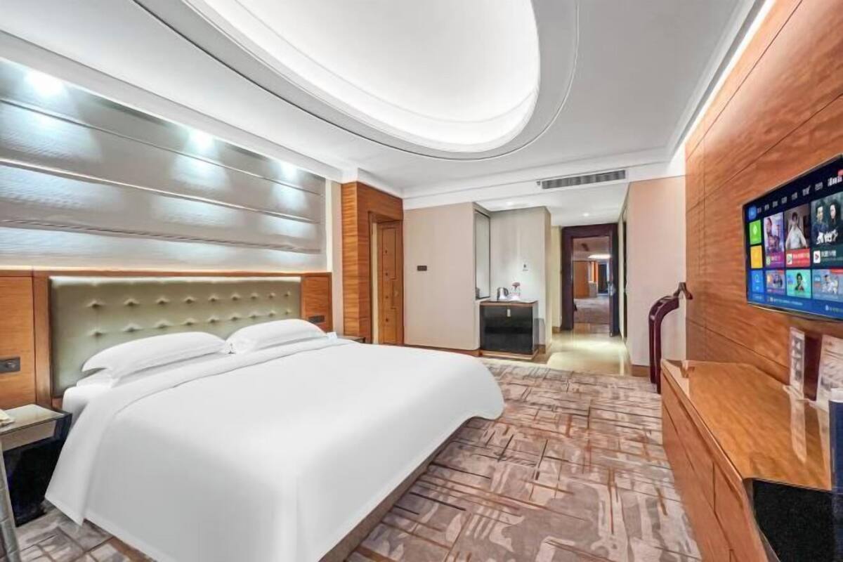A hotel room with a large bed, a wooden headboard, a built-in TV, and a patterned floor.