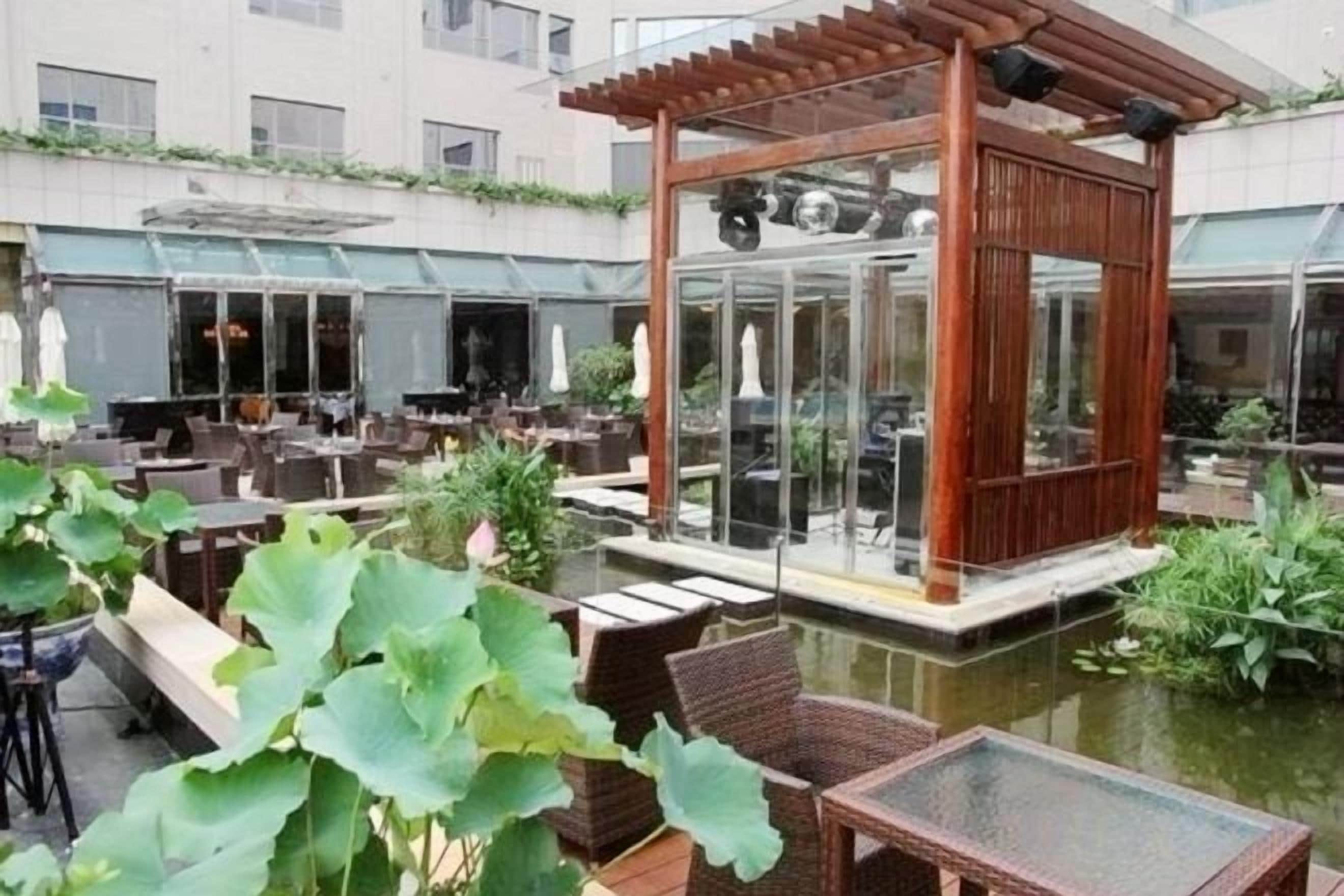 An outdoor seating area with tables and chairs, a wooden gazebo, and a pond.