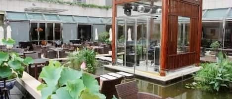 An outdoor seating area with tables and chairs, a wooden gazebo, and a pond.