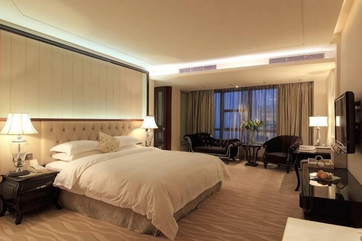 A hotel room with a large bed, a desk with a chair, a TV, and a small table with a plant.