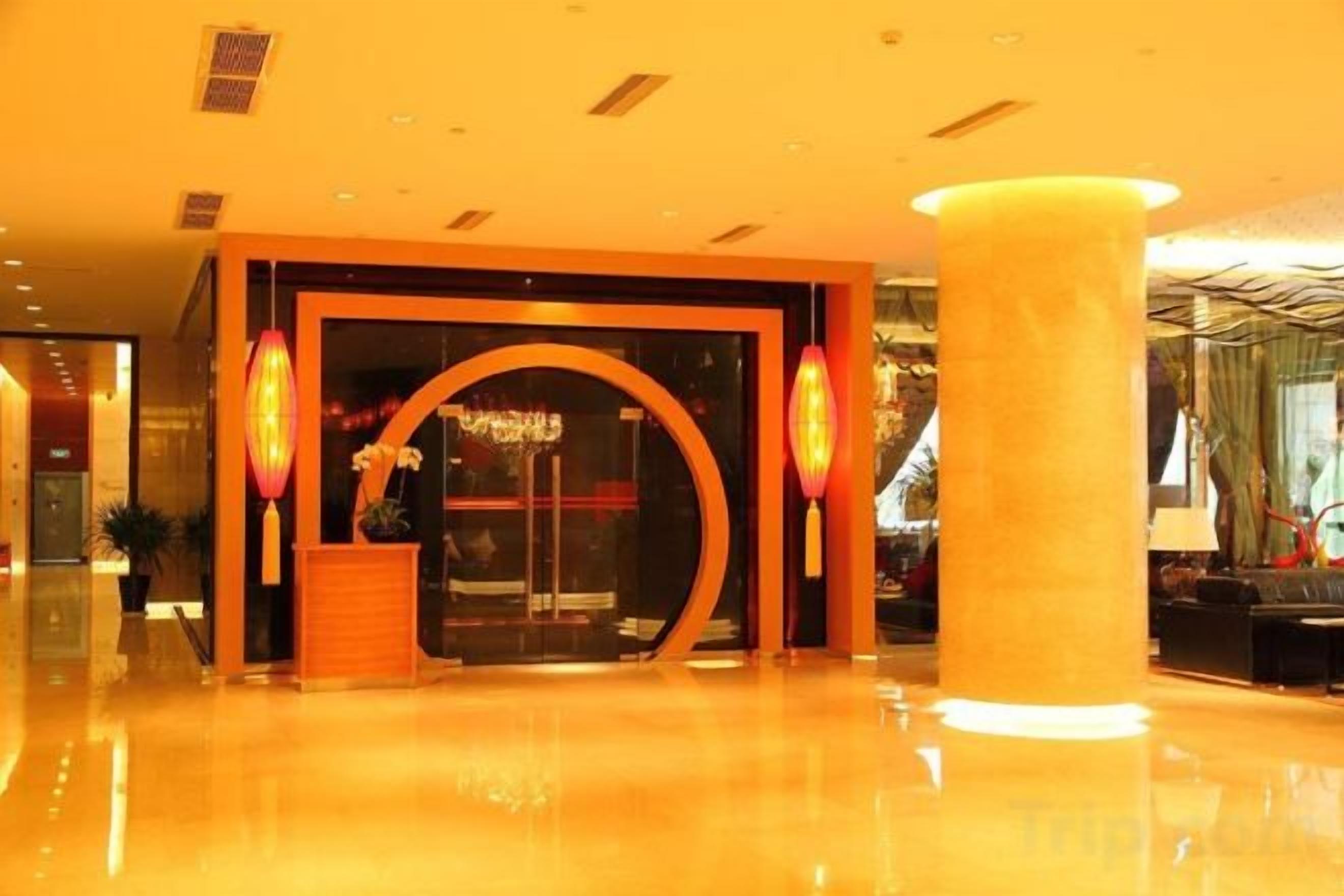 A hotel lobby with a reception desk, a large pillar, and a glass entrance.