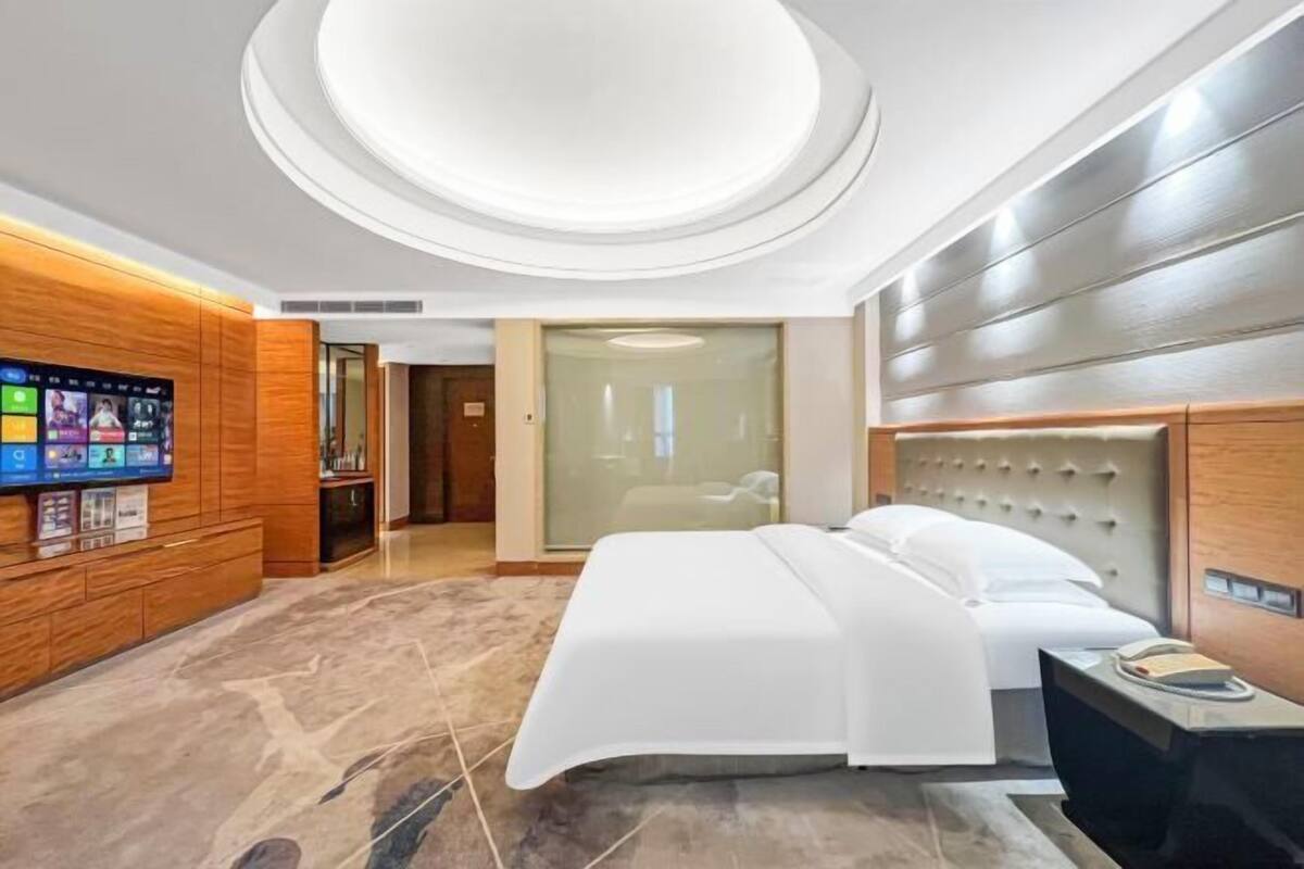A modern hotel room with a large bed, a flat-screen TV mounted on the wall, and a wooden panel design on the walls.
