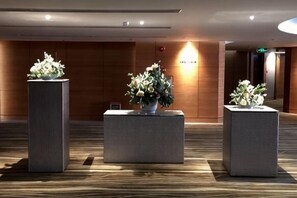 Un área de recepción con tres macetas cuadradas con flores, una pared de madera y un mostrador de recepción.