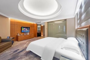 Une chambre d’hôtel moderne avec un grand lit, un téléviseur fixé sur un mur recouvert de panneaux en bois et une porte en verre donnant sur la salle de bain.