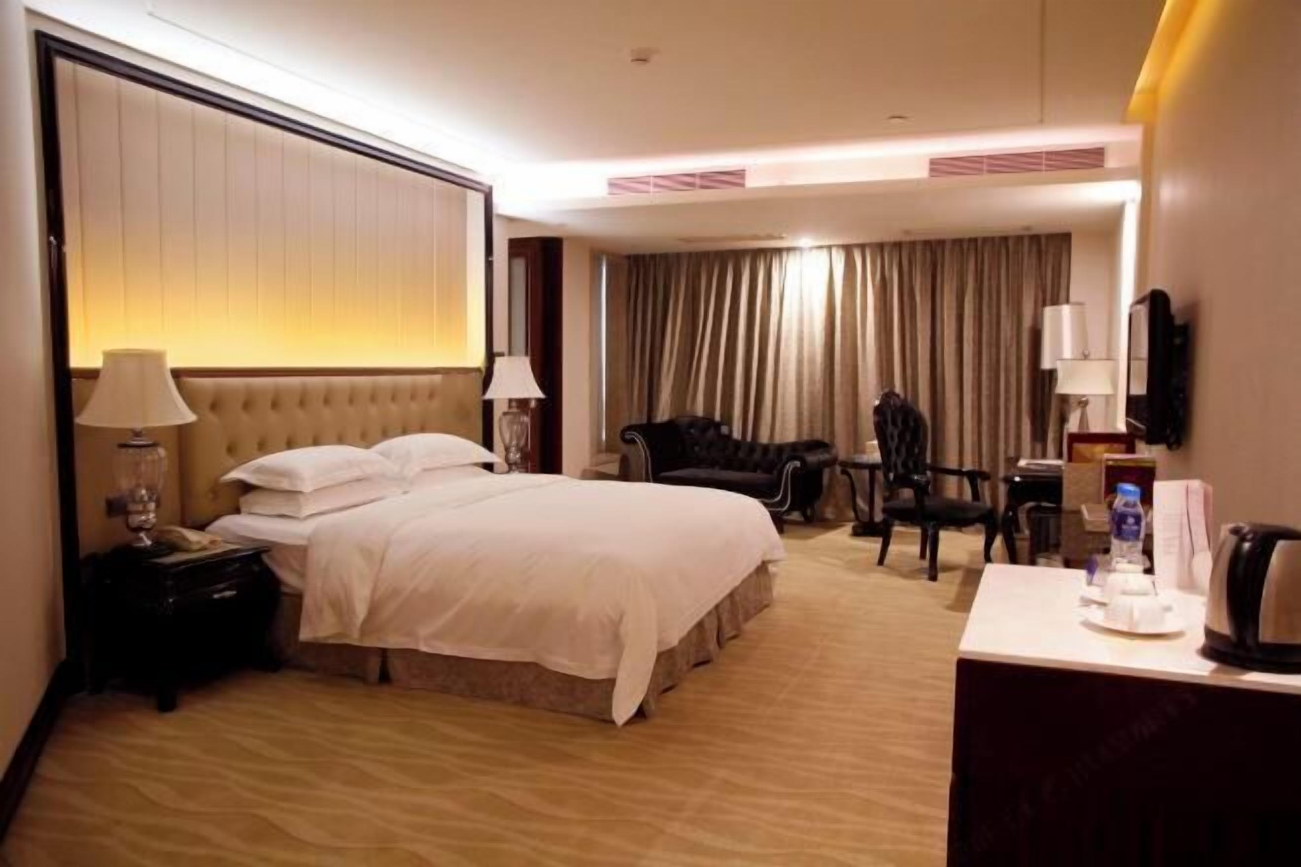Una habitación de hotel con una cama grande, mesitas de noche, un escritorio, una silla y un televisor.