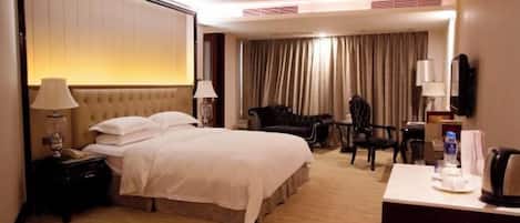 A hotel room with a large bed, bedside tables, a desk, a chair, and a TV.