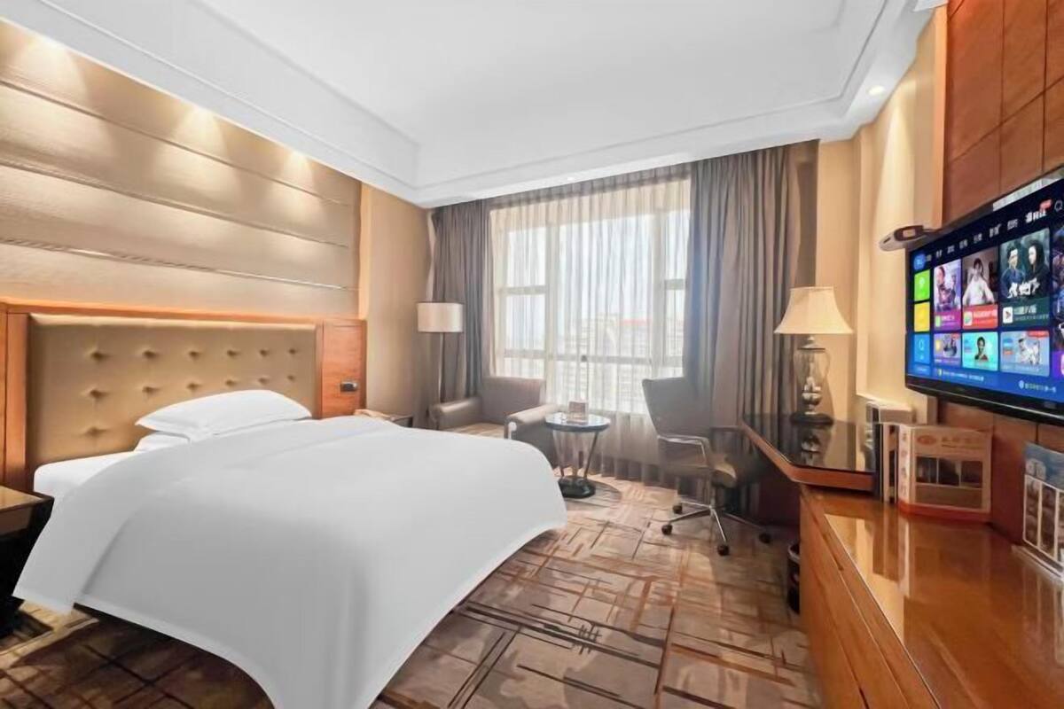 A hotel room with a large bed, a TV, a desk, and a chair.