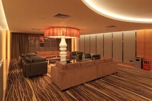 A hotel lobby with a large sofa, a coffee table, and a floor lamp. There are multiple seating options and a reception desk. - Lighting Era Hotel (Zhongshan)