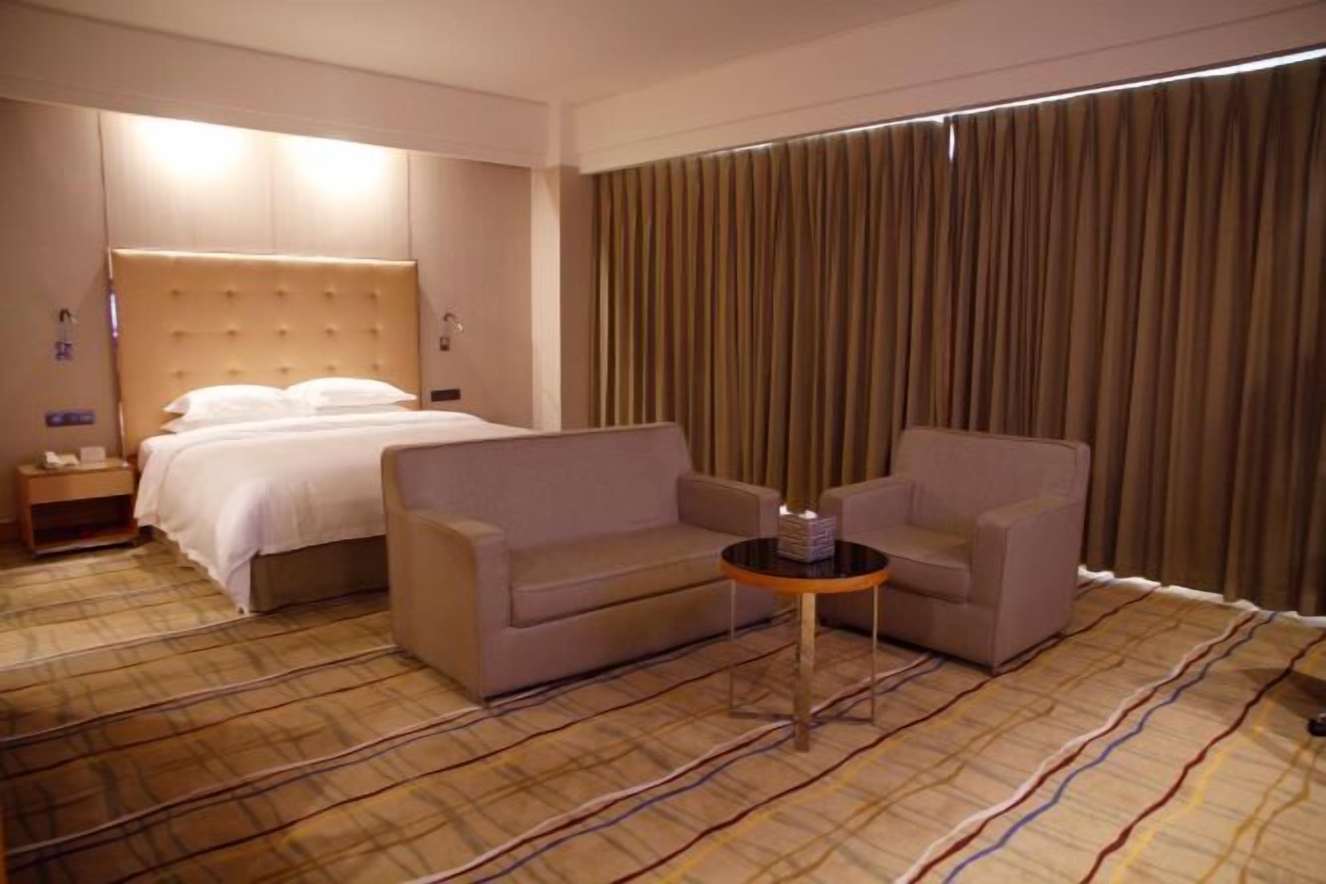 A hotel room with a bed, two armchairs, a small table, and a large window with curtains.