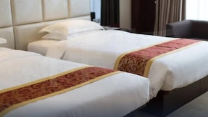A hotel room with two beds, each with white linens and a red decorative border. The room has a padded headboard and a dark-colored armchair. - Haili Business Hotel - Zhuhai (ZHUHAI)
