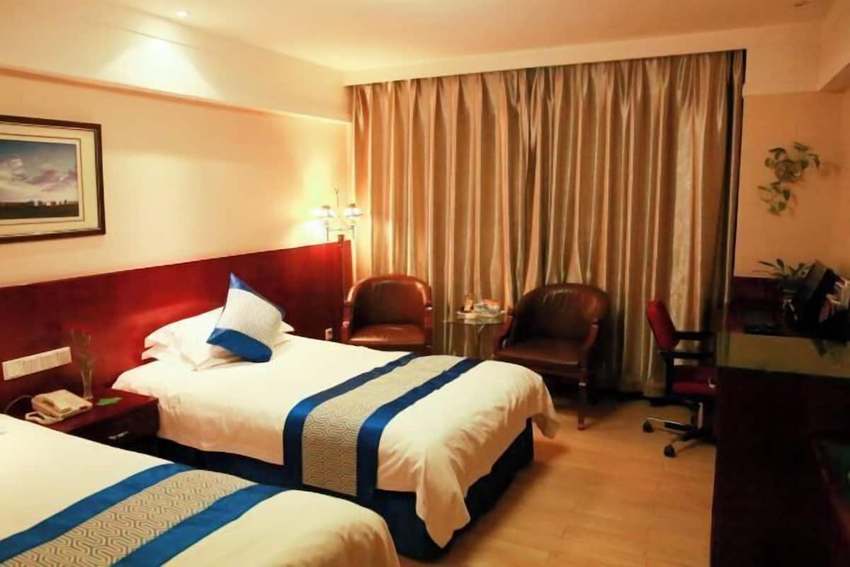 Habitación de hotel con dos camas, un escritorio, sillas, una mesita y una ventana con cortinas.