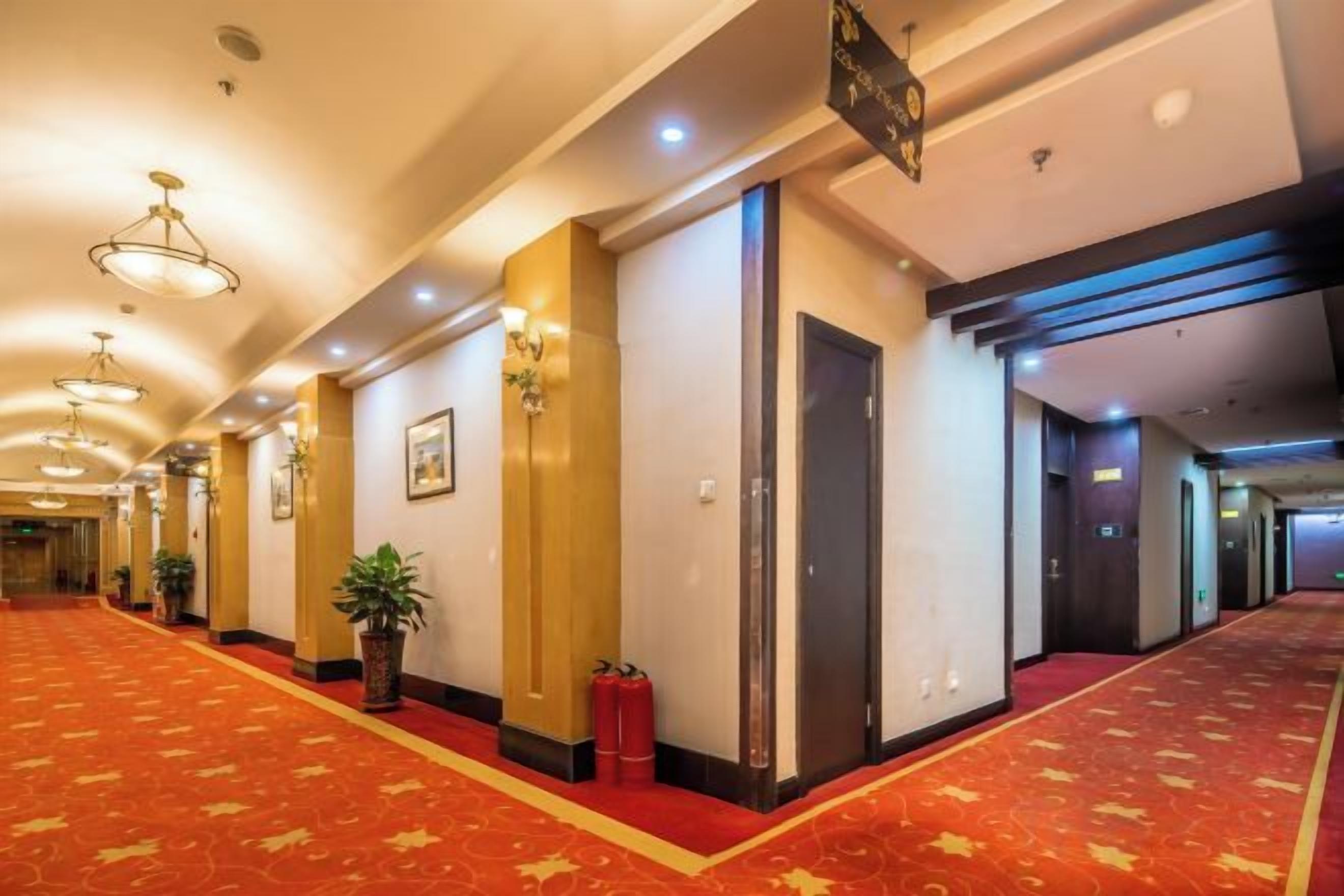 A hotel corridor with a red carpet, doors, and wall-mounted lights.