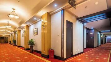 A hotel corridor with a red carpet, doors, and wall-mounted lights.