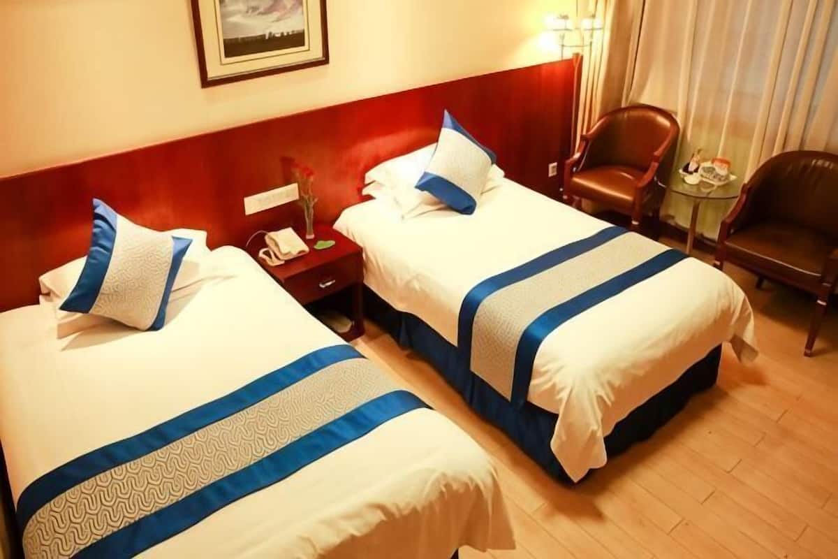 Habitación de hotel con dos camas, cabecera de madera, mesita de noche con un teléfono y un florero, y una pequeña mesa con una silla.