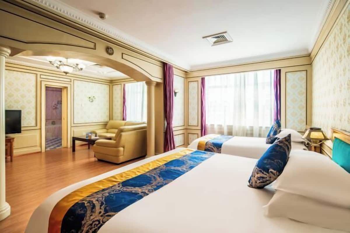 Una habitación de hotel con dos camas, un sofá, un televisor y un ventanal con cortinas.