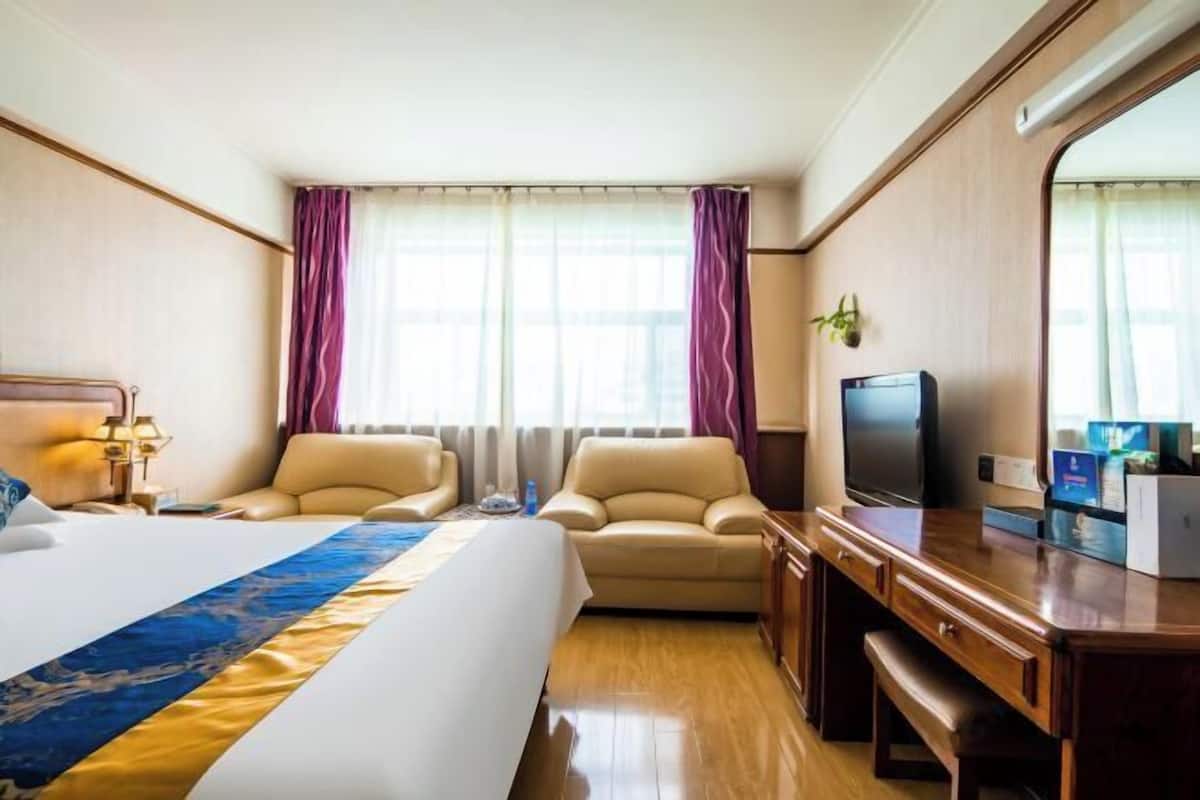 Habitación de hotel con una cama grande, dos sillones, un escritorio con televisor y una ventana con cortinas.