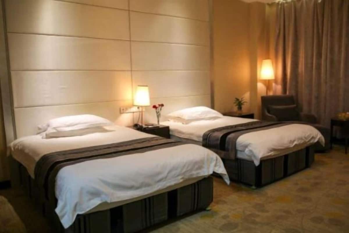 Una habitación de hotel con dos camas, una silla, una mesita de noche con lámpara y una ventana con cortinas.