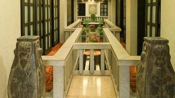 A corridor with a marble floor, stone balustrades, and a central railing.