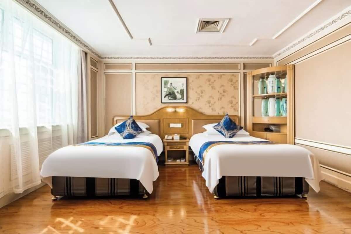 Habitación de hotel con dos camas, suelo de madera, estante con botellas montado en la pared y un cuadro enmarcado sobre las camas.