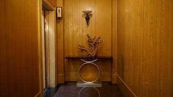 A wooden interior hallway with a door, a wall-mounted light fixture, and a small table with a vase.