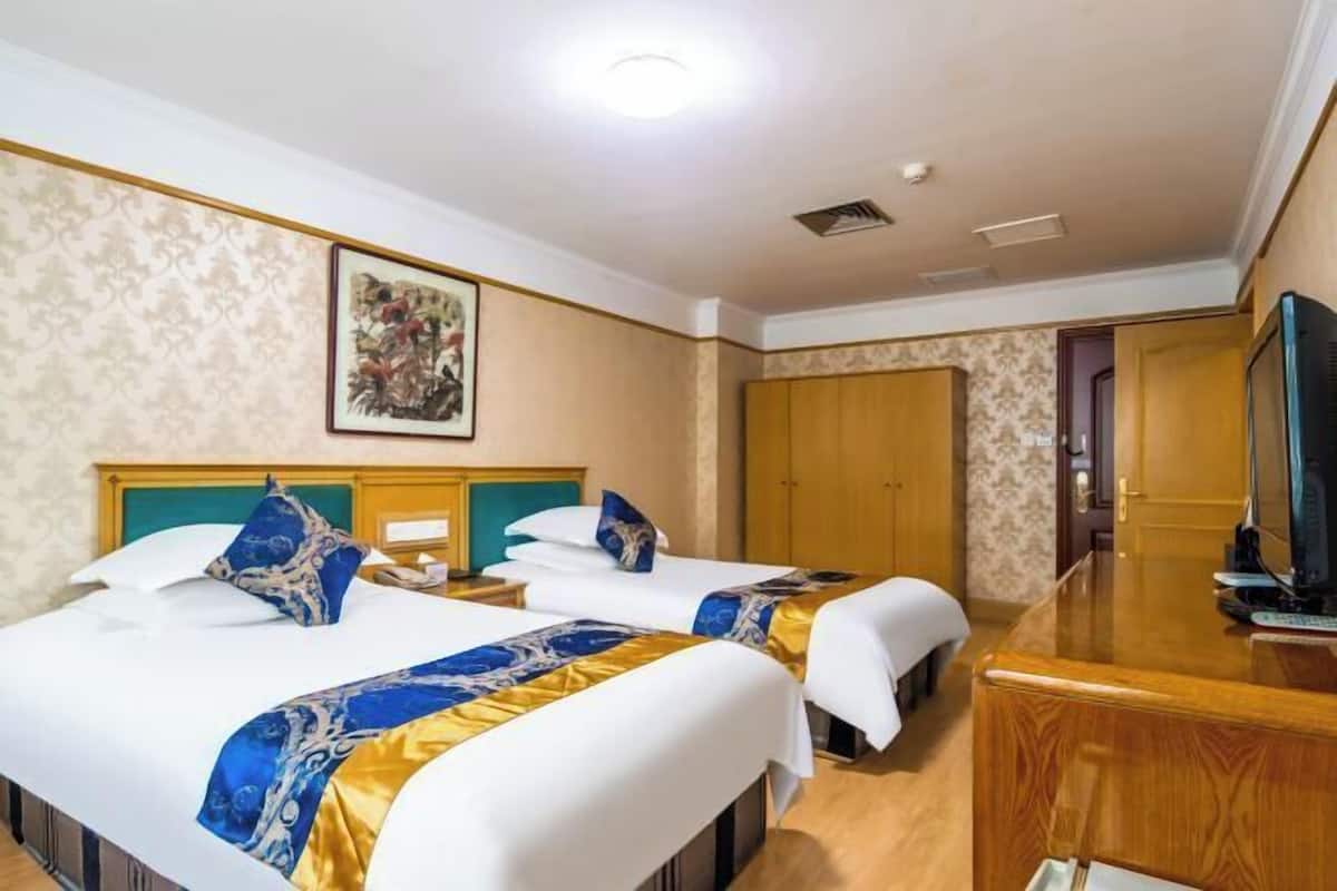 Una habitación de hotel con dos camas, un escritorio, un televisor y una puerta que da a otra habitación.