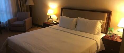 A hotel room with a large bed, two bedside tables, a chair, and a lamp.