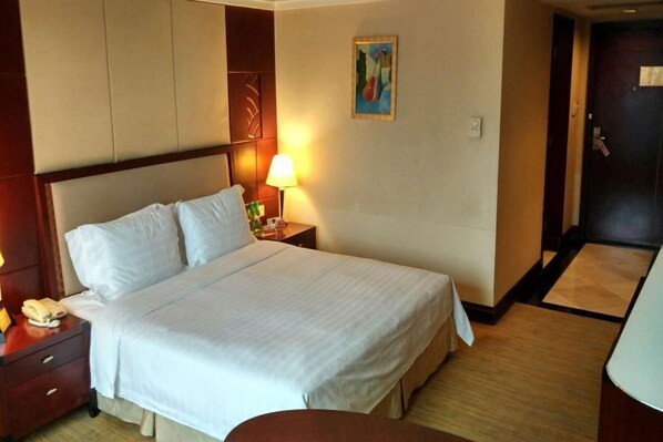 Une chambre d’hôtel avec un grand lit, une lampe de chevet, une table de chevet avec un téléphone et une porte sur le côté droit.