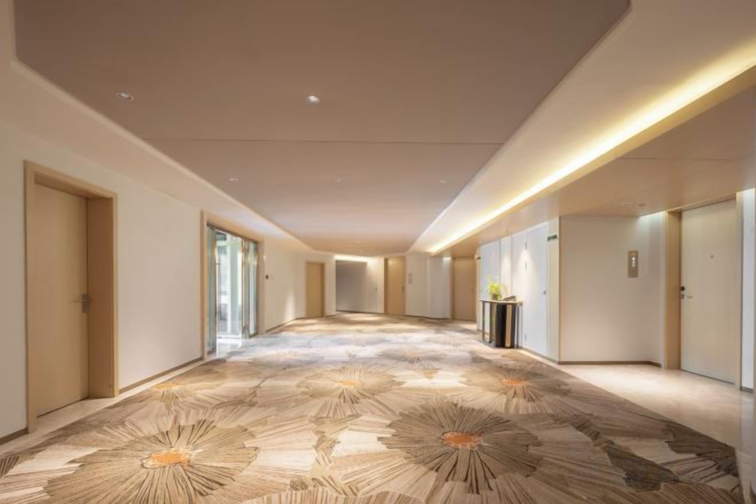 A hotel corridor with a patterned carpet, doors on both sides, and a long hallway.