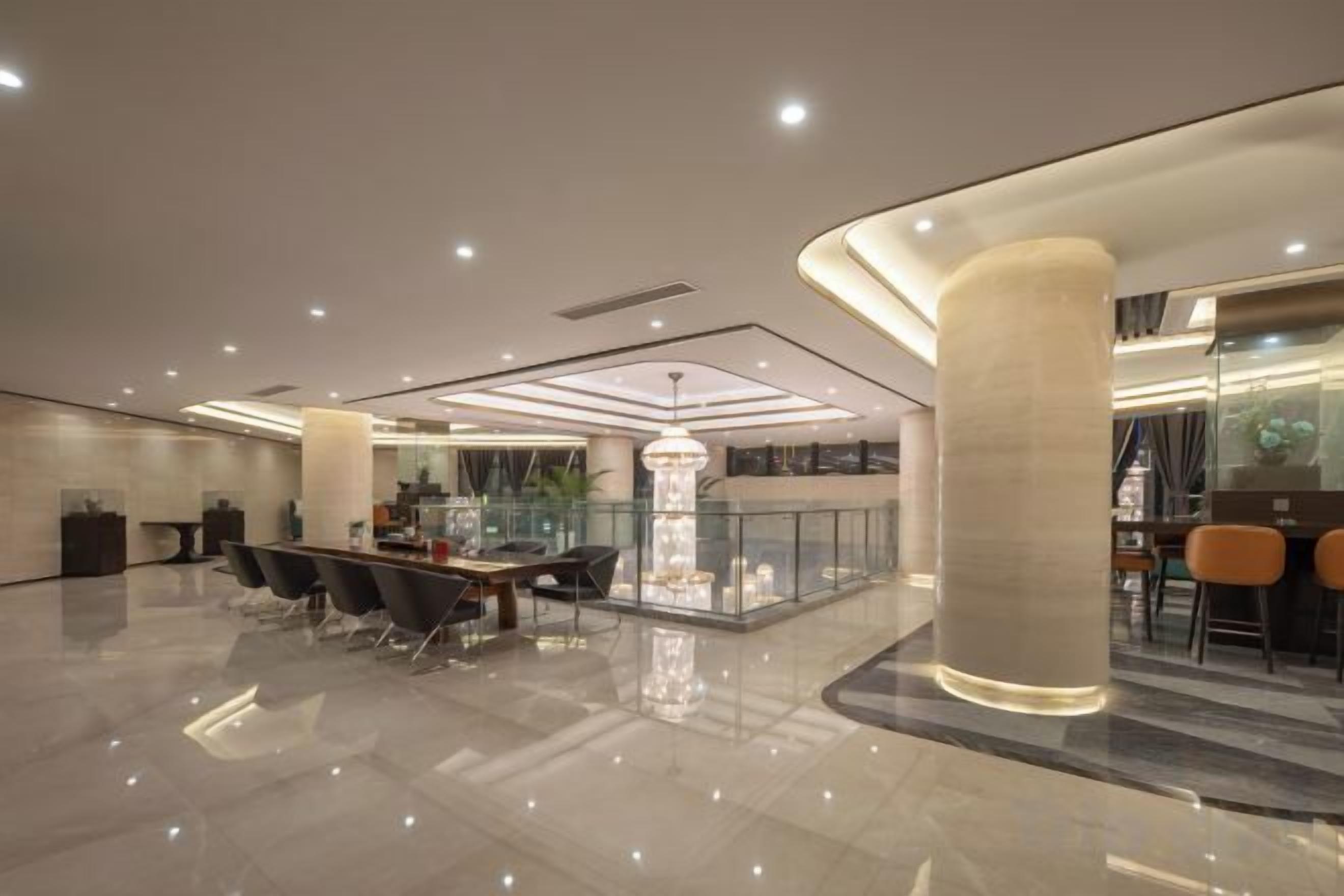 A spacious lobby with a central dining area, a reception desk, and a modern chandelier.