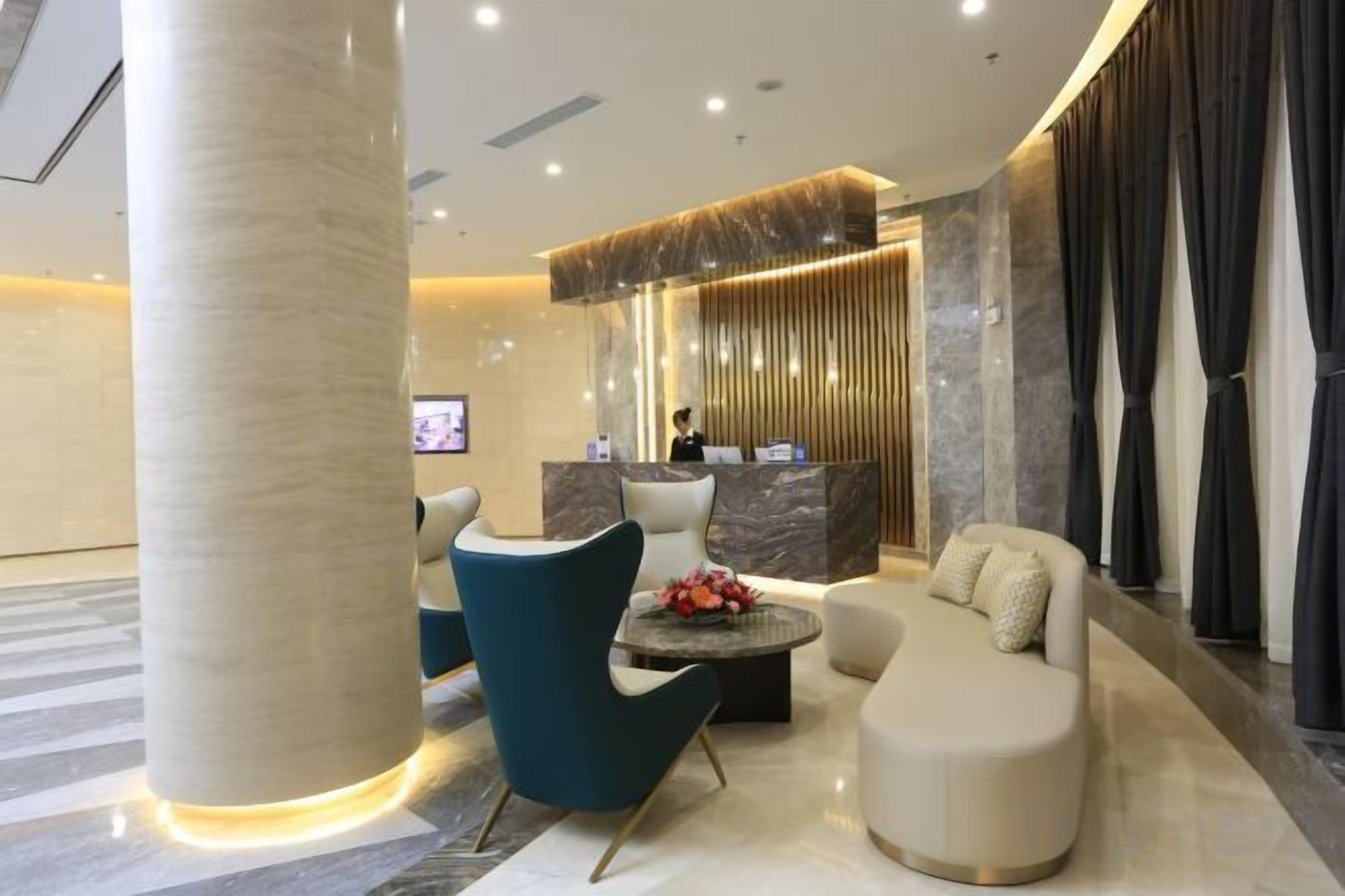 A modern hotel lobby with a reception desk, seating area, and a large column.