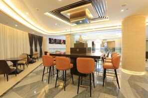 Un espace de restauration moderne dans un hôtel, comprenant un bar, des sièges et une vue sur la cuisine.