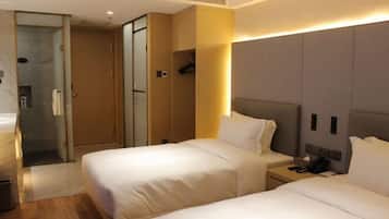 A hotel room with two beds, a bedside table with a phone, and a shower area.