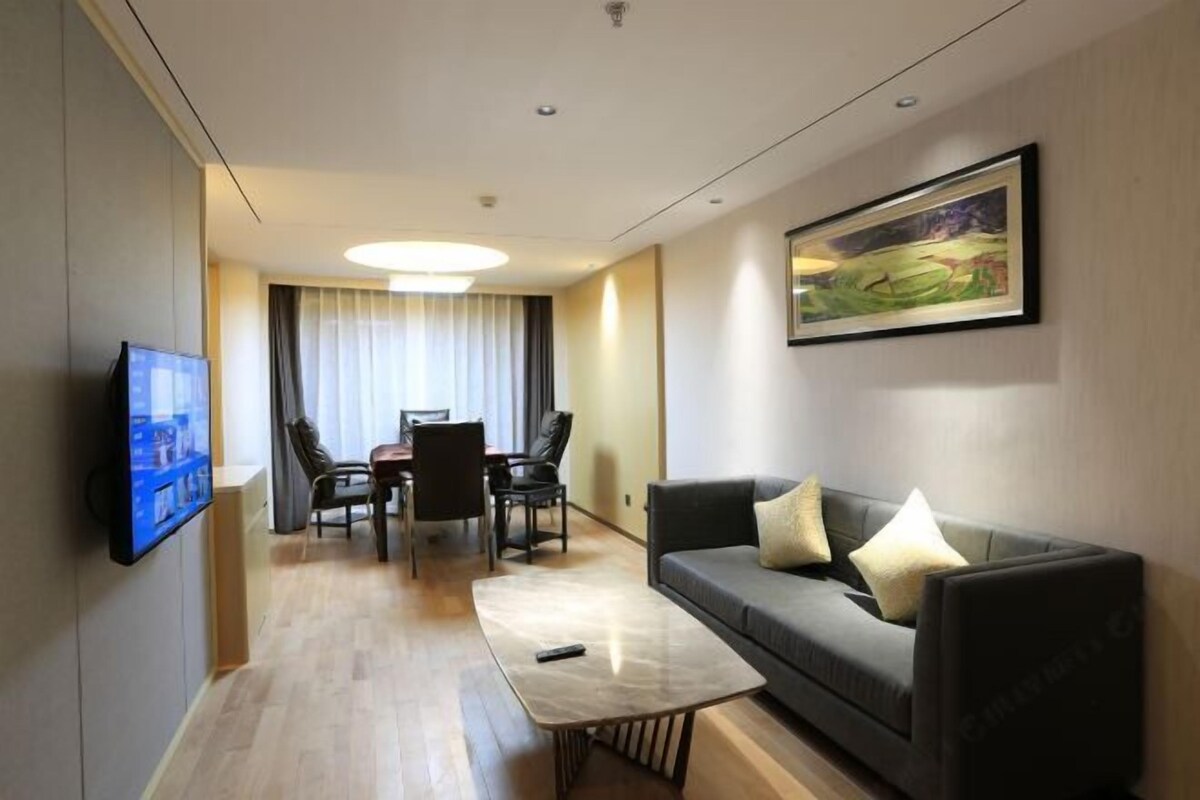 Une chambre d’hôtel moderne équipée d’un téléviseur à écran plat, d’un canapé, d’une table basse, d’un coin repas avec des chaises et d’un tableau au mur.