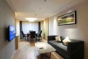 Ein modernes Hotelzimmer mit Flachbildfernseher, einer Sitzecke, einem Couchtisch, einer Essecke mit Stühlen und einem Bild an der Wand.