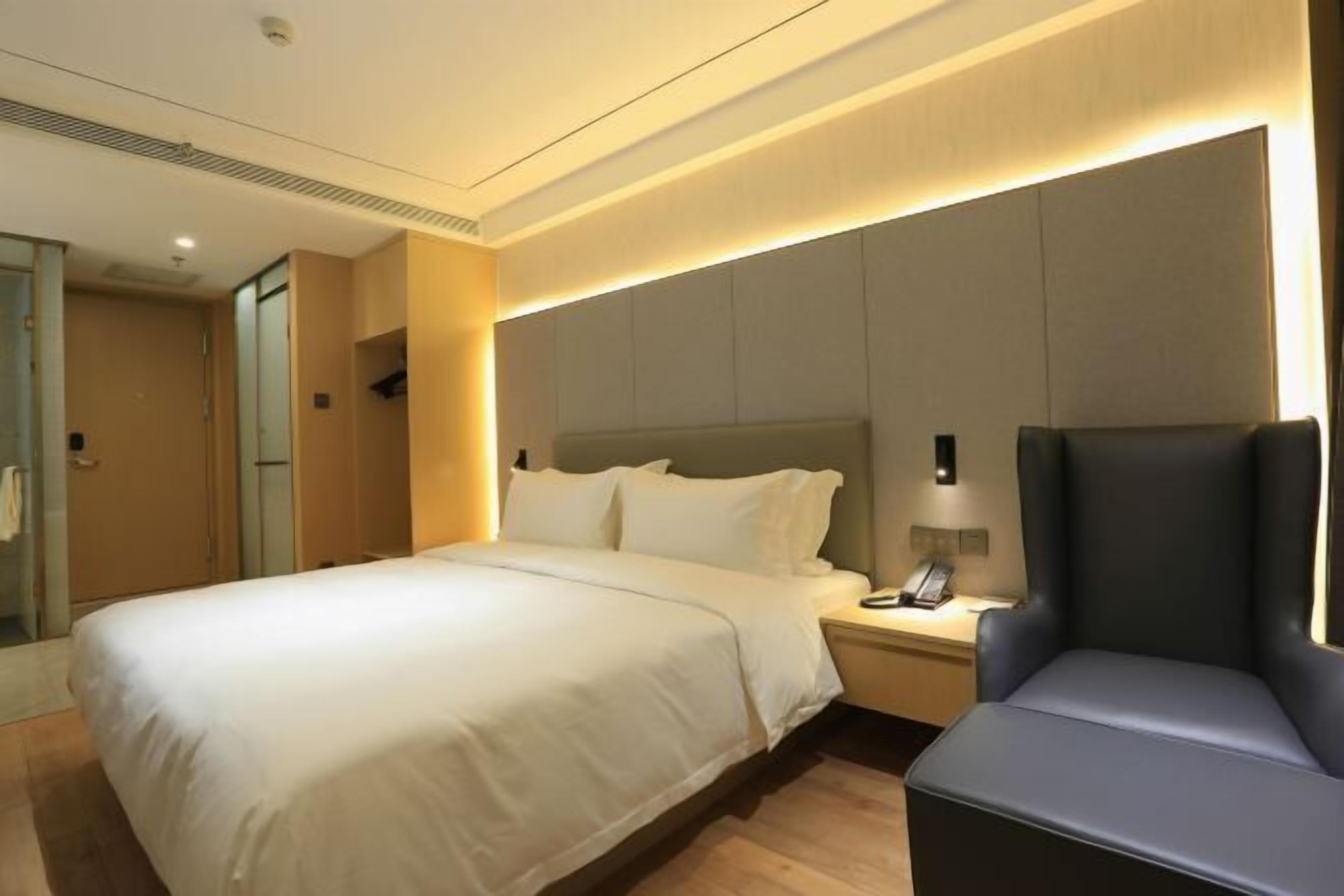 A hotel room with a bed, bedside table, chair, and a wall-mounted phone.