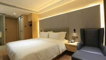 A hotel room with a bed, bedside table, chair, and a wall-mounted phone.