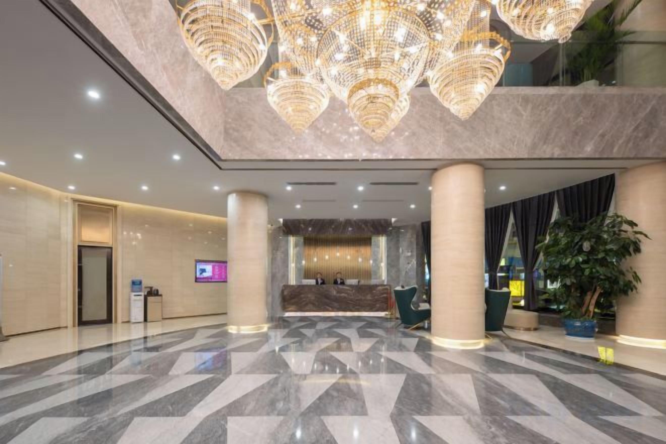 A hotel lobby with a reception desk, large chandeliers, and a polished marble floor.