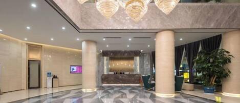 A hotel lobby with a reception desk, large chandeliers, and a polished marble floor.