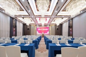 Une salle de conférence avec des rangées de tables et de chaises, un grand écran à l’avant et de somptueux lustres.