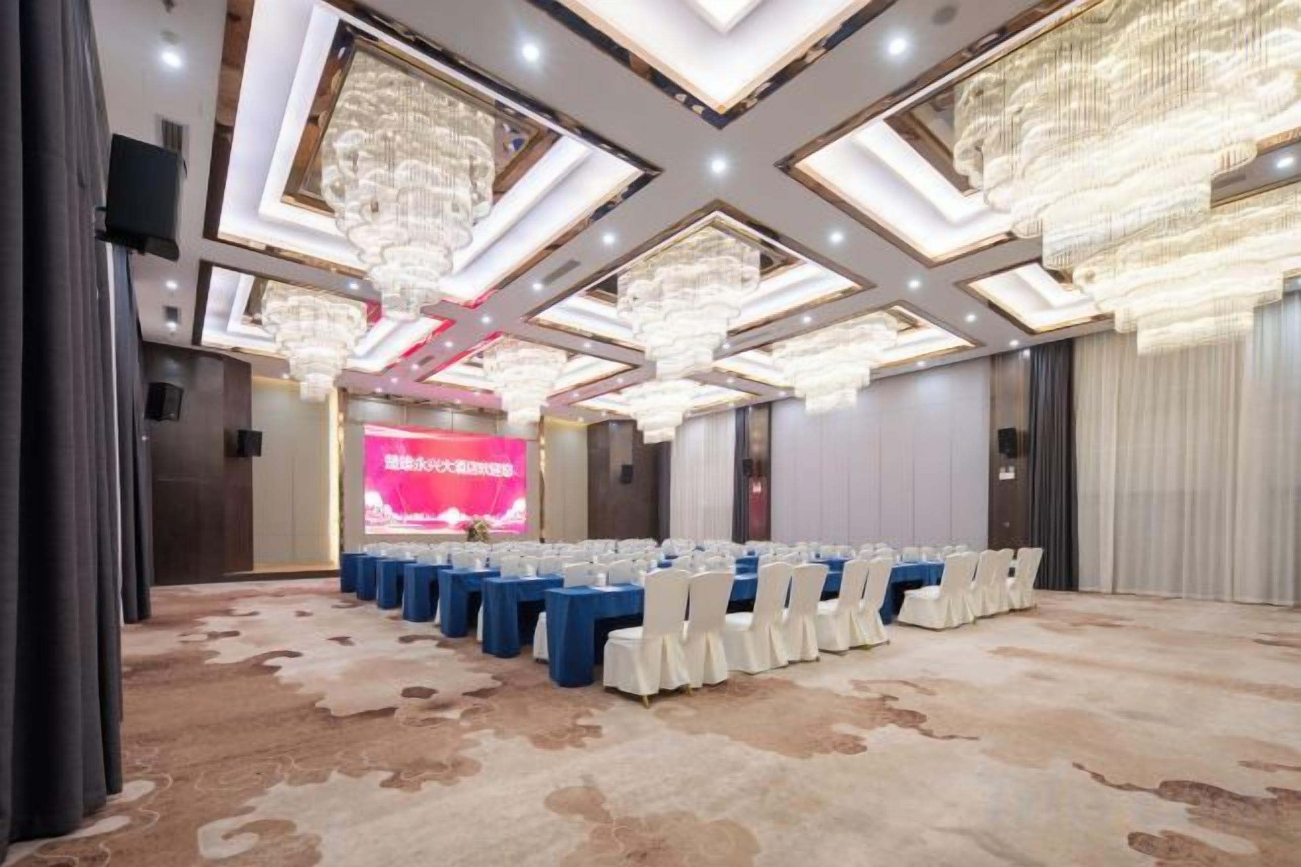 Une salle de conférence avec une scène, des rangées de tables et des chaises.