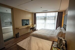 Une chambre d’hôtel moderne équipée d’un grand lit, d’un bureau avec une chaise, d’une télévision et d’un mini-bar.