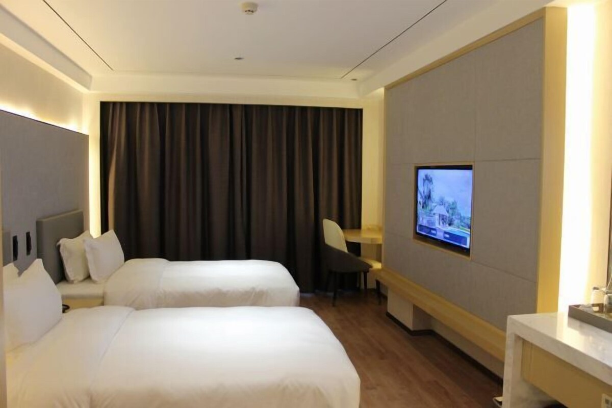 Une chambre d’hôtel avec deux lits, un bureau, une chaise et un téléviseur fixé au mur.