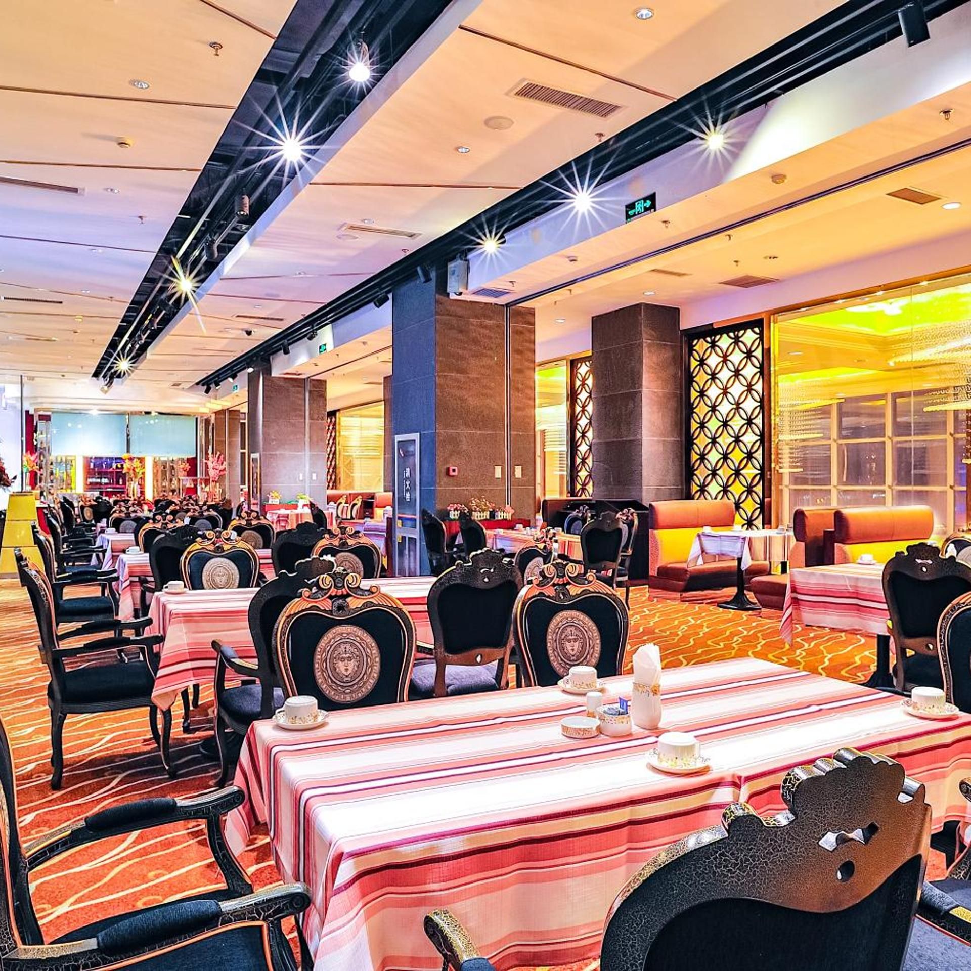 A hotel dining area with multiple tables and chairs, a patterned carpet, and a modern ceiling design.