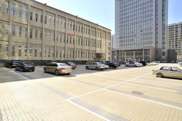 A parking lot with several cars, a building with multiple windows, and a tall skyscraper in the background.
