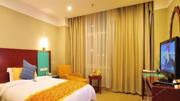 A hotel room with a bed, a television, a chair, and a small table with a lamp. - Uiles Hotel (Hohhot)