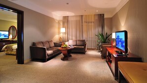 A hotel room with a sofa set, a coffee table with fruit, a TV, and a bed with a patterned bedspread. - Uiles Hotel (Hohhot)