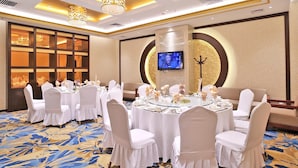 A banquet hall with round tables, white chairs, and chandeliers. - Uiles Hotel (Hohhot)
