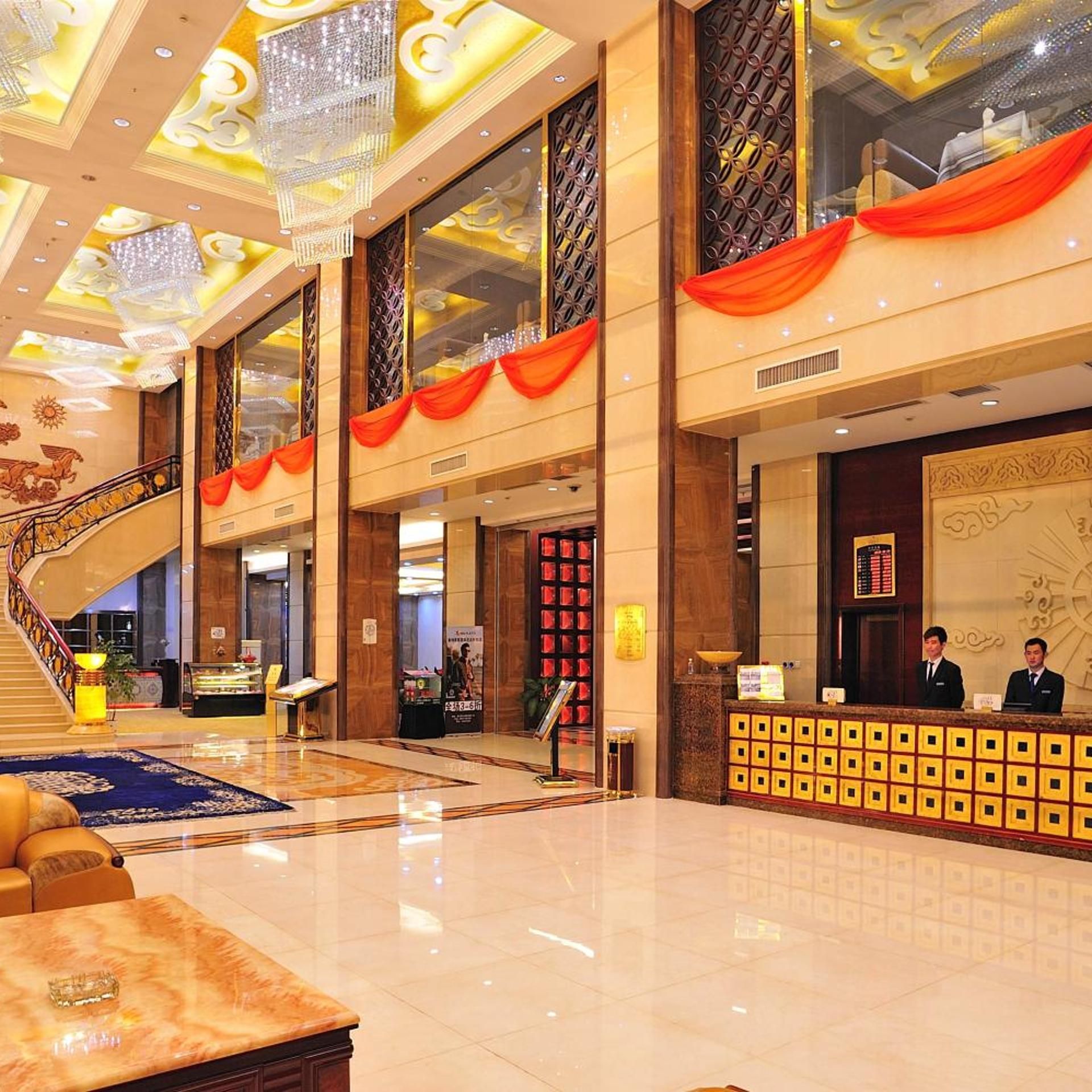 A spacious lobby with a grand staircase, a reception desk, and a decorative wall.