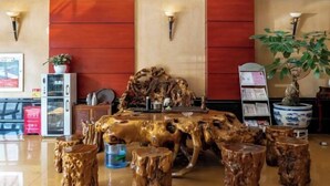 Una habitación con una mesa de madera como centro, taburetes de madera, una planta en maceta y una estantería.