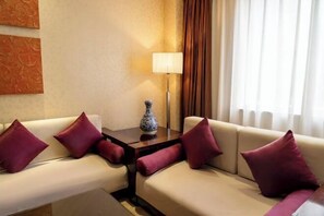 A hotel room with a beige sofa set, a small table with a vase, and a lamp. - Golden Palace Hotel (Kunming)